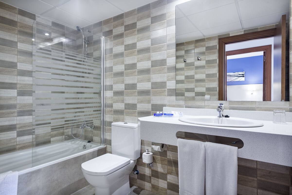 Une salle de bain moderne avec une douche à parois de verre, des toilettes et un lavabo surmonté d’un miroir.