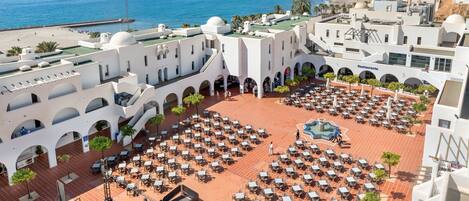 A rooftop terrace with numerous tables and chairs, a restaurant, and a view of the sea.