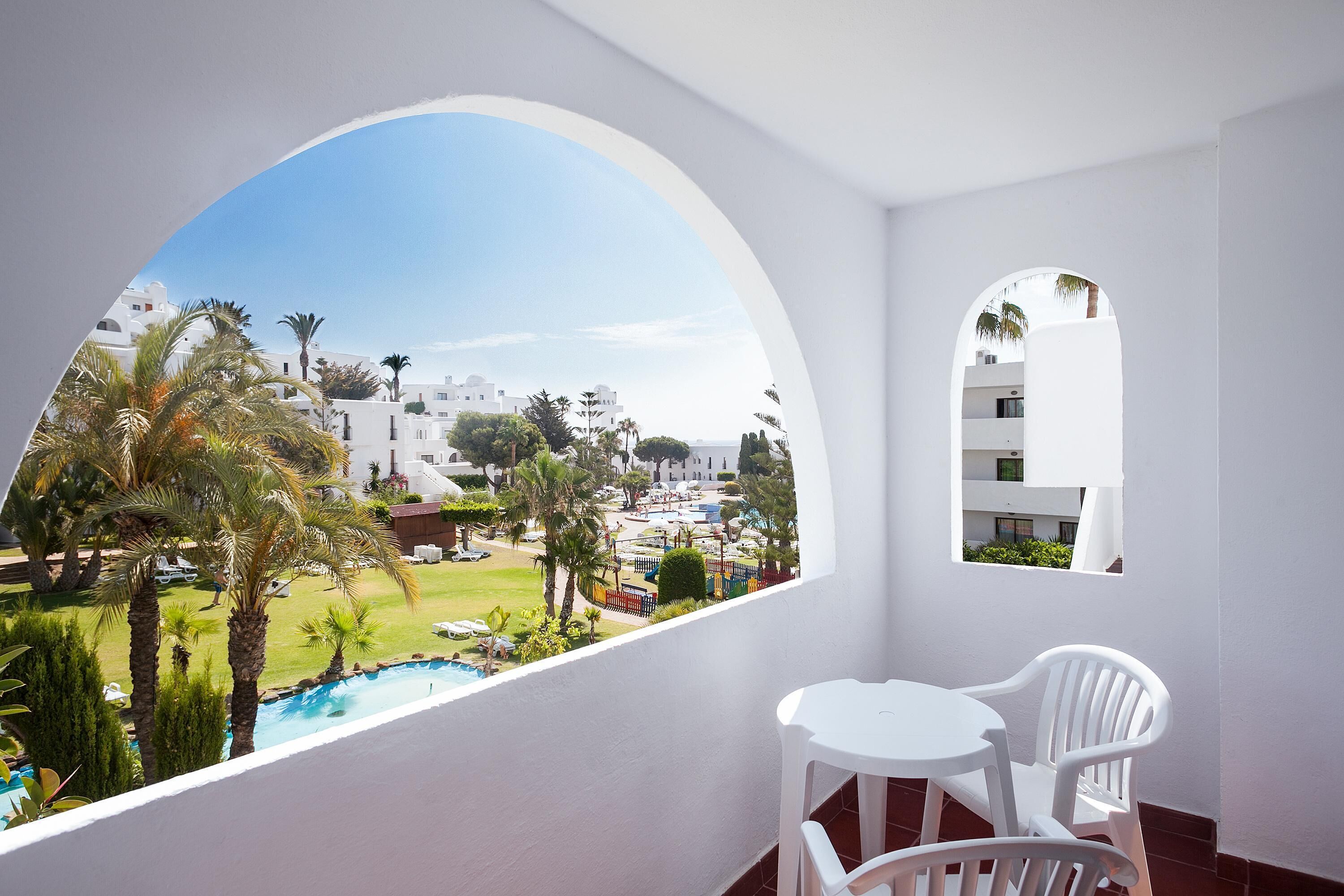 A balcony with a view of a pool, palm trees, and white buildings.