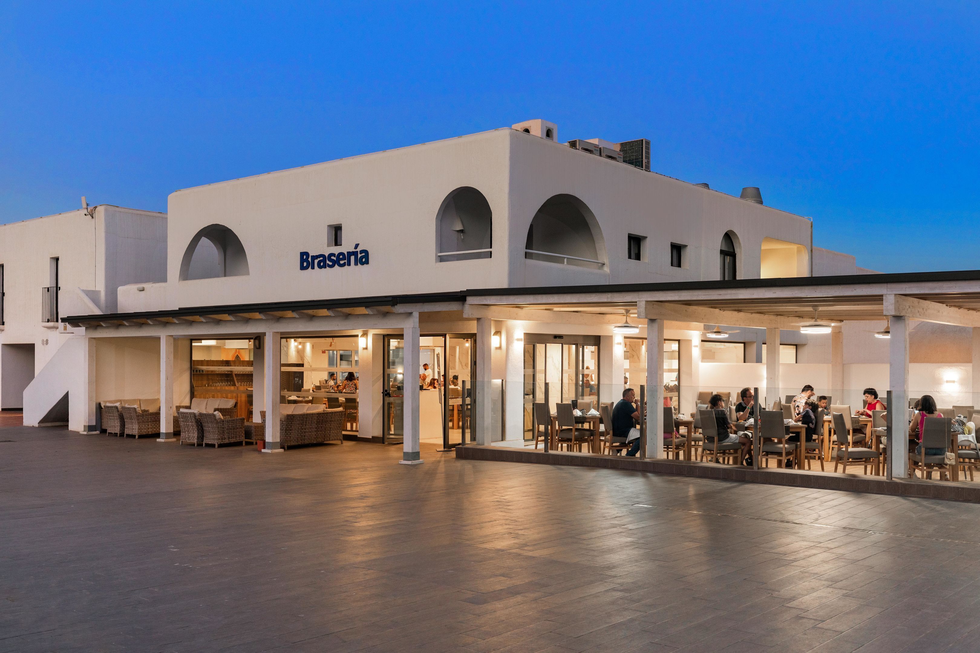 A modern building with the name 'Brasserie' on the facade, featuring an outdoor seating area with tables and chairs.