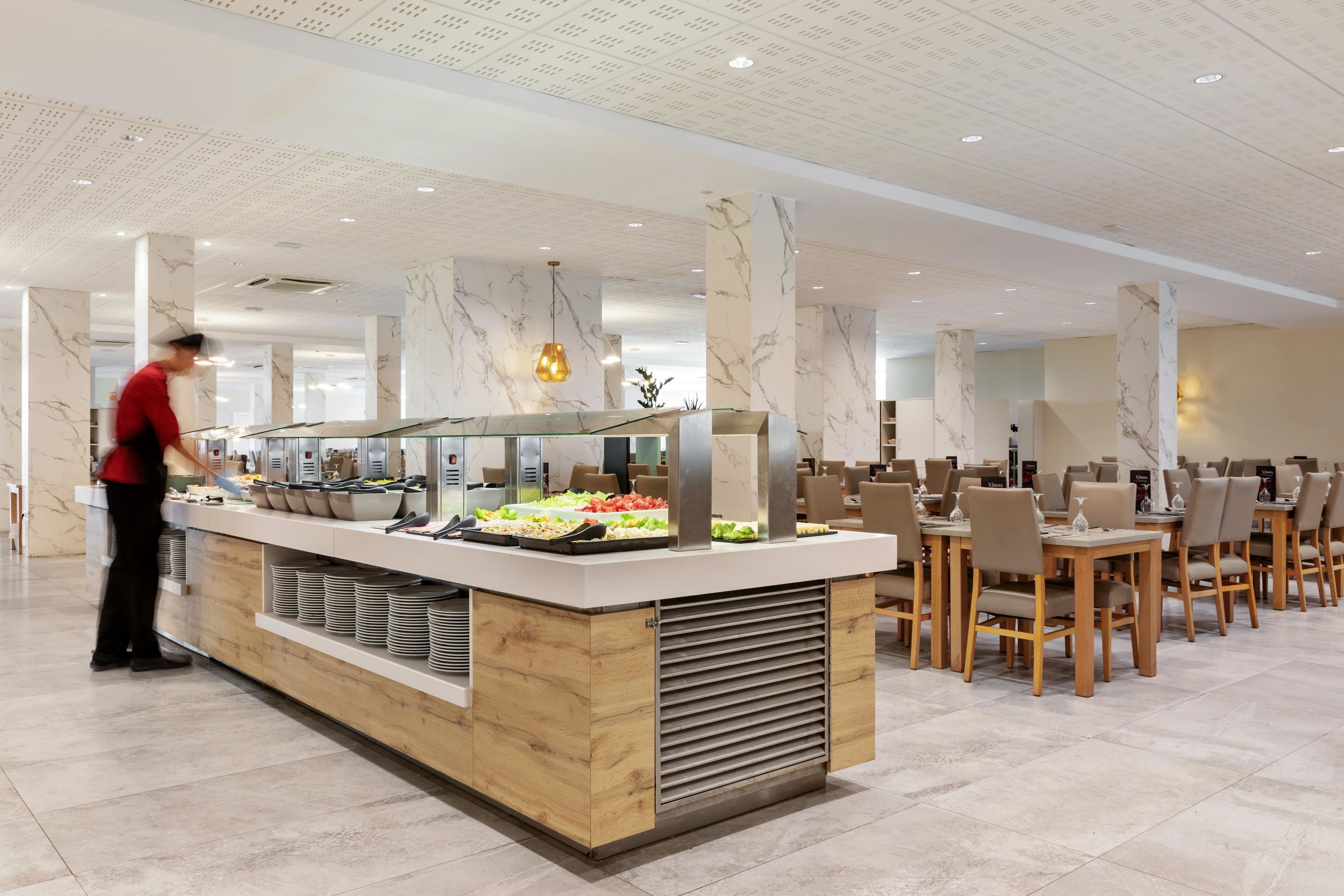 Ein Buffetbereich mit Marmorsäulen, einer zentralen Servicestation und mehreren Esstischen mit Stühlen.