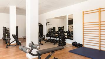 Un gimnasio con equipos de ejercicio, una banca y un muro con espejos.