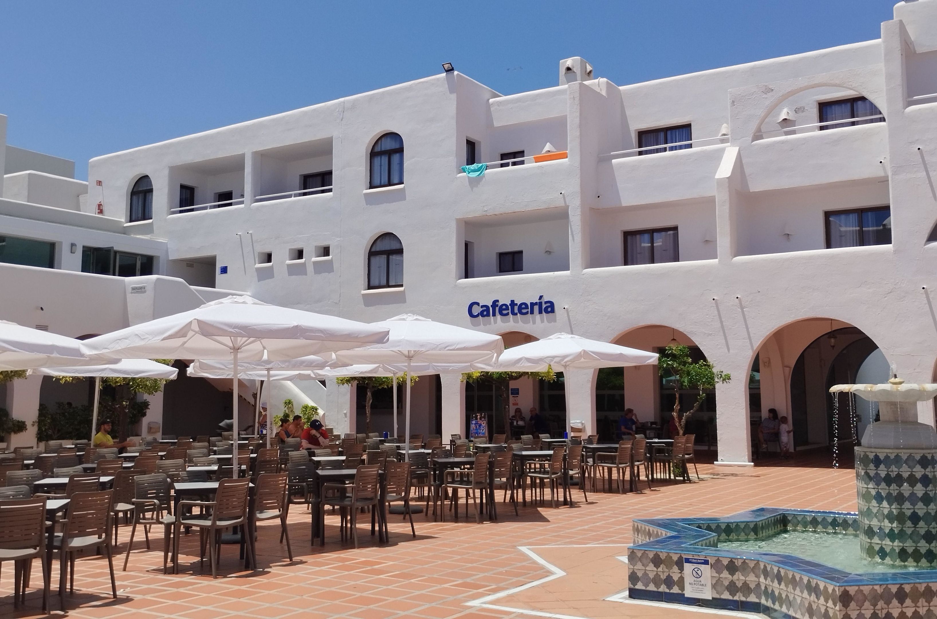 Edifici blanc amb un rètol que diu "Cafetería" i terrassa amb ombrelles.