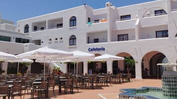 Edifici blanc amb un rètol que diu "Cafetería" i terrassa amb ombrelles.