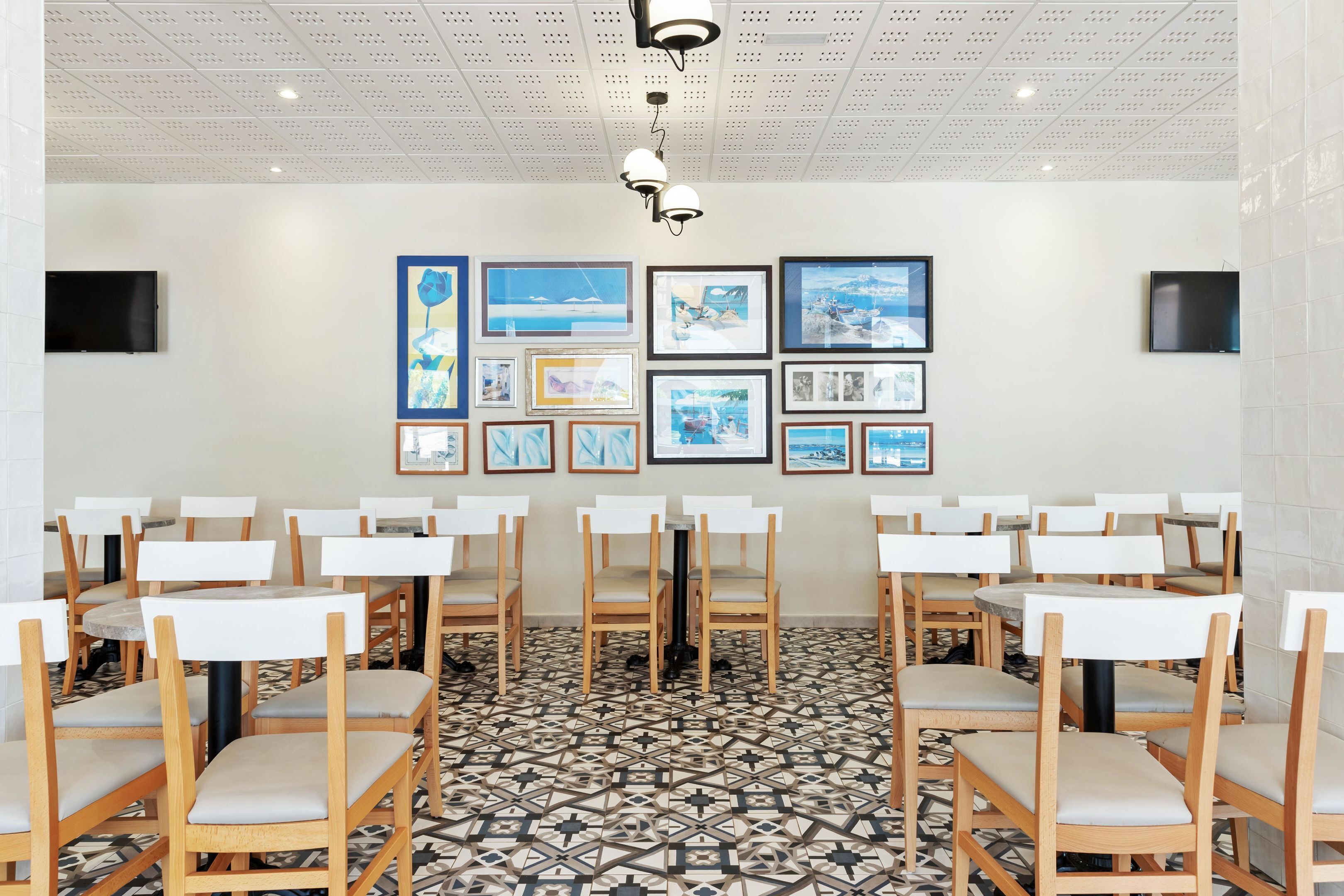 Un comedor con mesas y sillas redondas, un piso con diseño y obras de arte enmarcadas en las paredes.