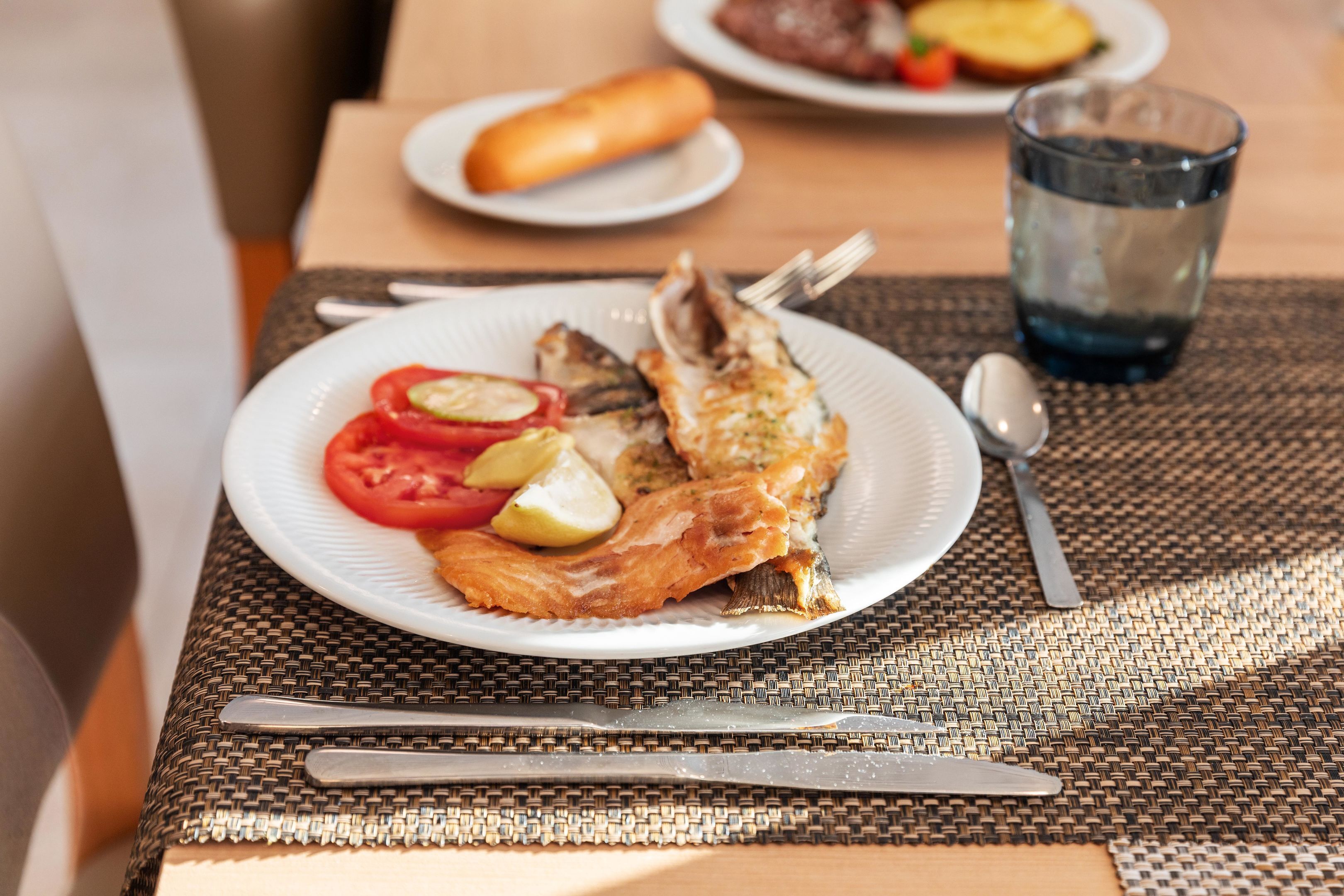 A dining table with a plate of grilled fish, lemon wedges, and tomato slices.
