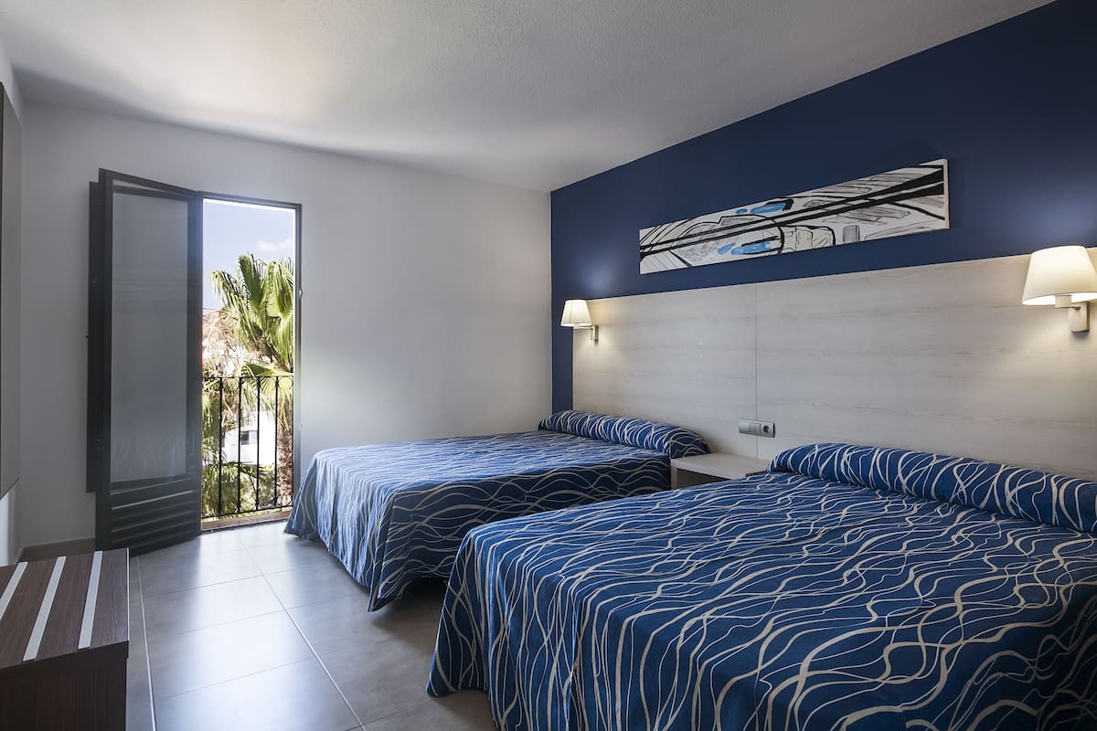 Une chambre d’hôtel avec deux lits, une grande fenêtre et une vue sur des palmiers.