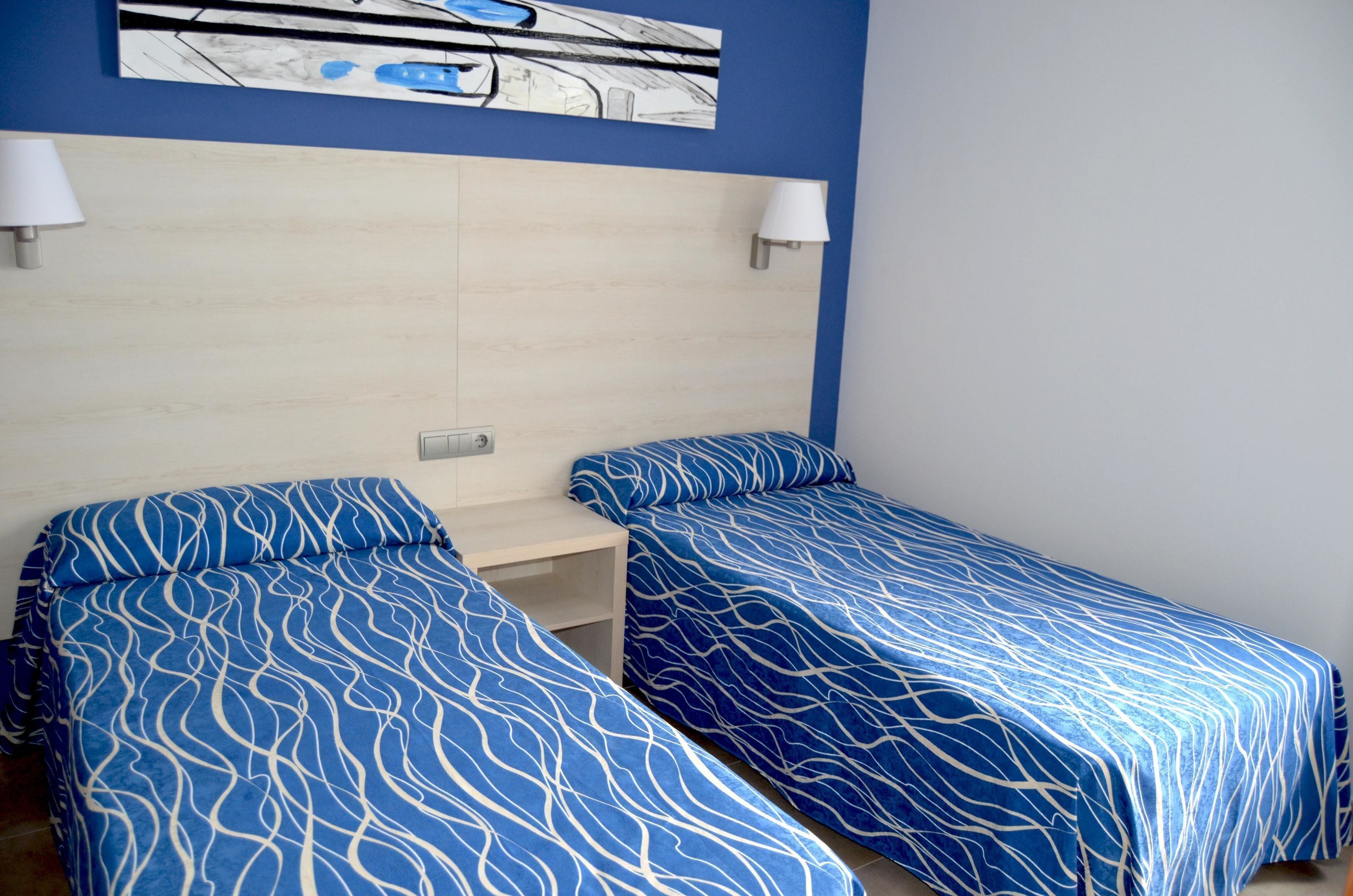 A hotel room with two single beds, a wooden headboard, and a wall-mounted lamp.