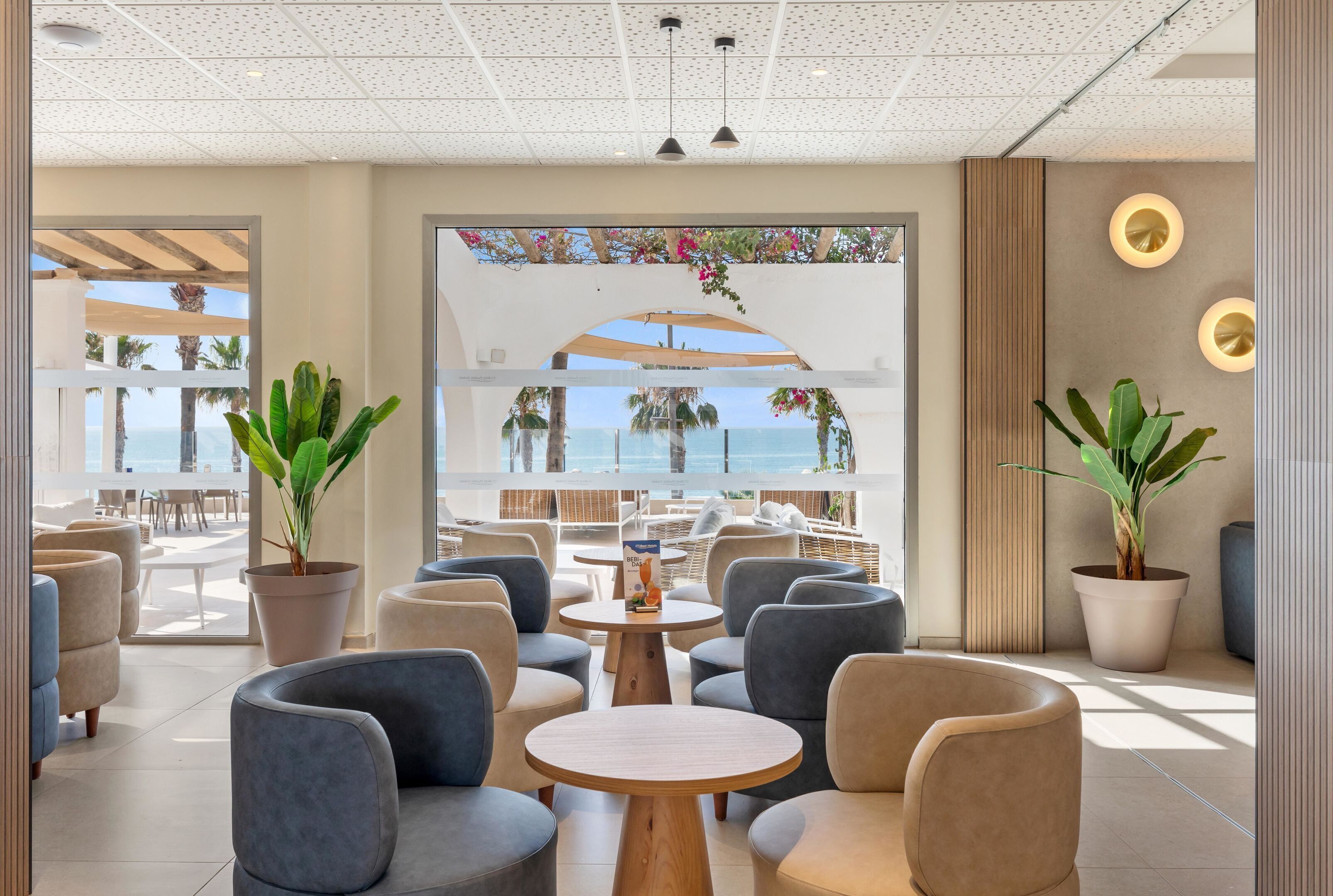 Un espacio lounge moderno con mesas redondas y asientos cómodos, con vistas a un hermoso paisaje marino.