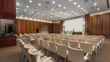 Un salón de conferencias con filas de sillas, un atril y una pantalla grande.
