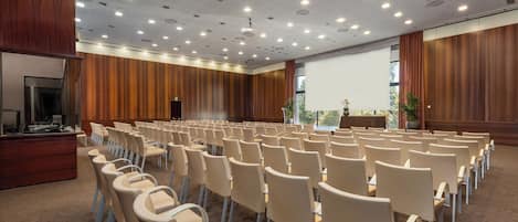 A conference room with rows of chairs, a podium, and a large screen.