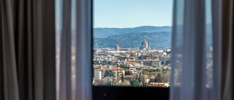 A cityscape through a window with curtains, featuring a prominent dome and a tall tower.