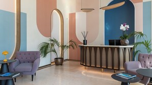 A modern reception area with a curved reception desk, two plush armchairs, a potted plant, and a small table with a book. - DoubleTree by Hilton Florence Metropole (Florence)