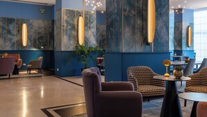 A modern lobby with blue walls, a central seating area with sofas and chairs, and a decorative light fixture. - DoubleTree by Hilton Florence Metropole (Florence)