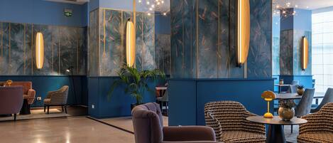 A modern lobby with blue walls, a central seating area with sofas and chairs, and a decorative light fixture.