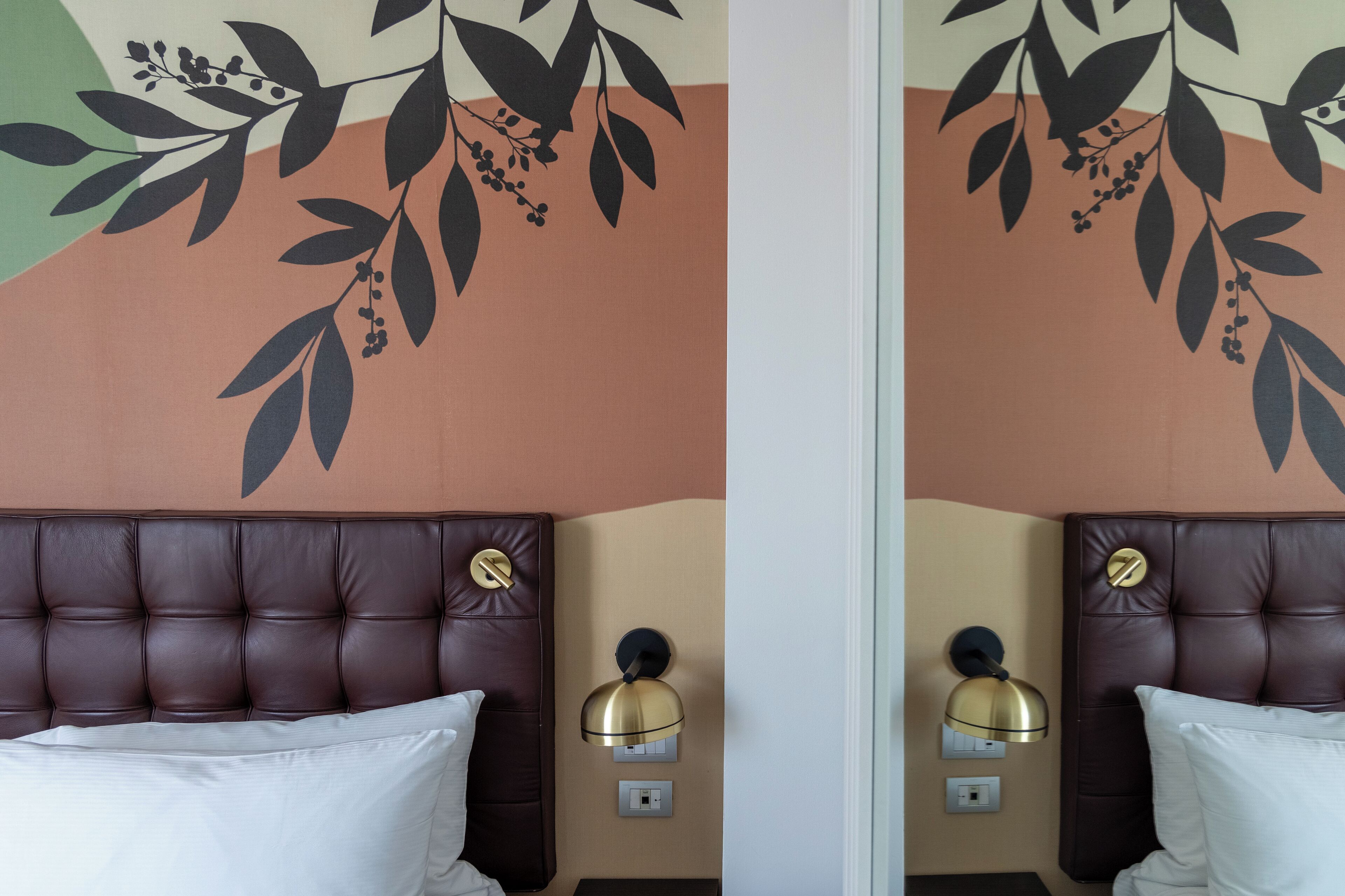 A hotel room with a brown leather headboard, a white pillow, and a wall-mounted lamp.