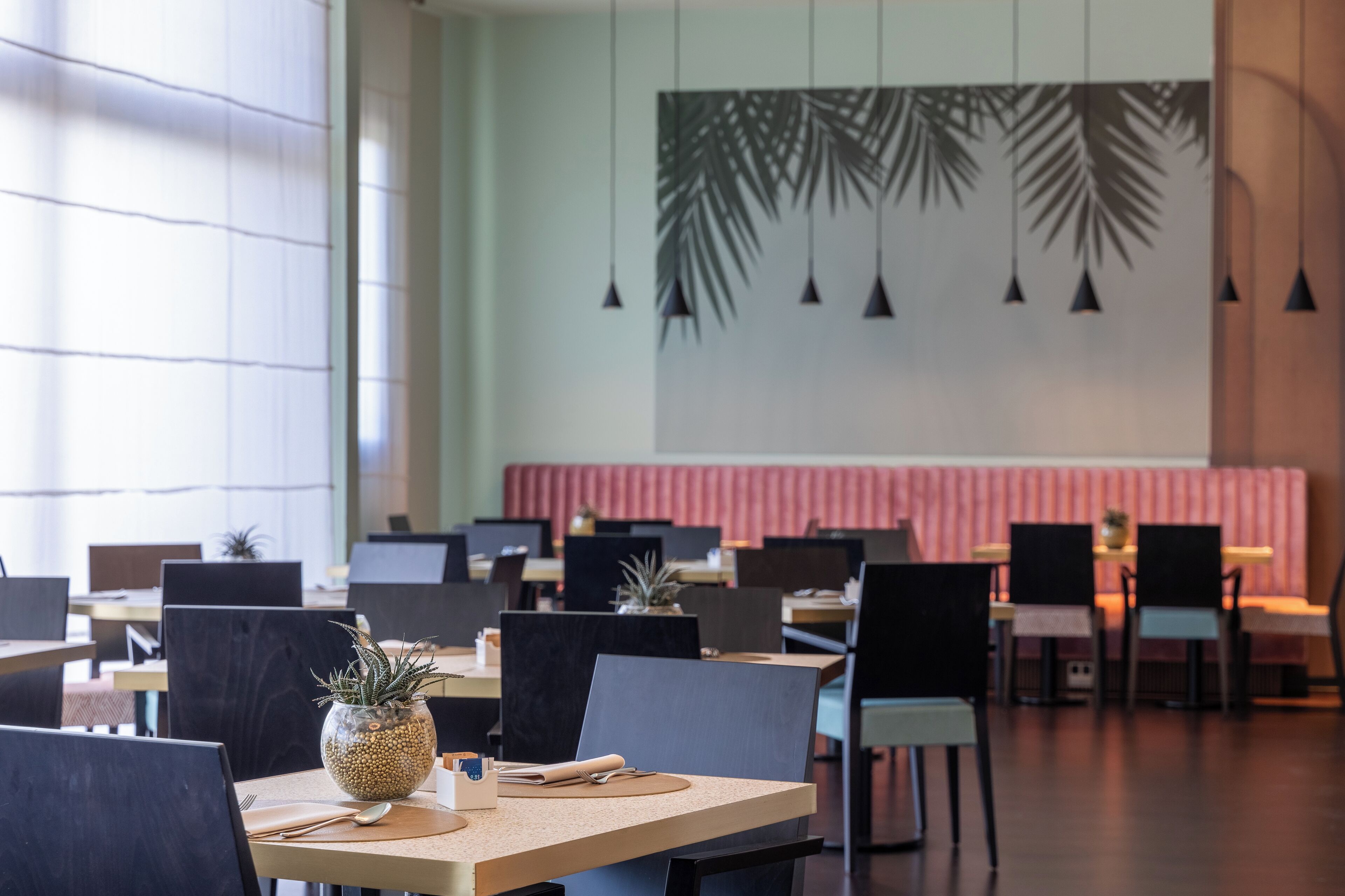 A modern restaurant interior with multiple tables and chairs, a decorative wall with hanging lights, and a seating area with a pink backdrop.