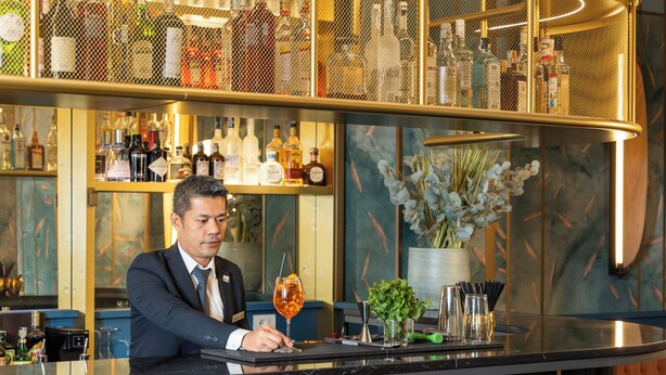 A bartender at a bar with a variety of liquor bottles in the background. - DoubleTree by Hilton Florence Metropole (Florence)
