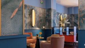 A modern lobby with blue walls, a red sofa, a pink armchair, and a small table with a lamp. - DoubleTree by Hilton Florence Metropole (Florence)