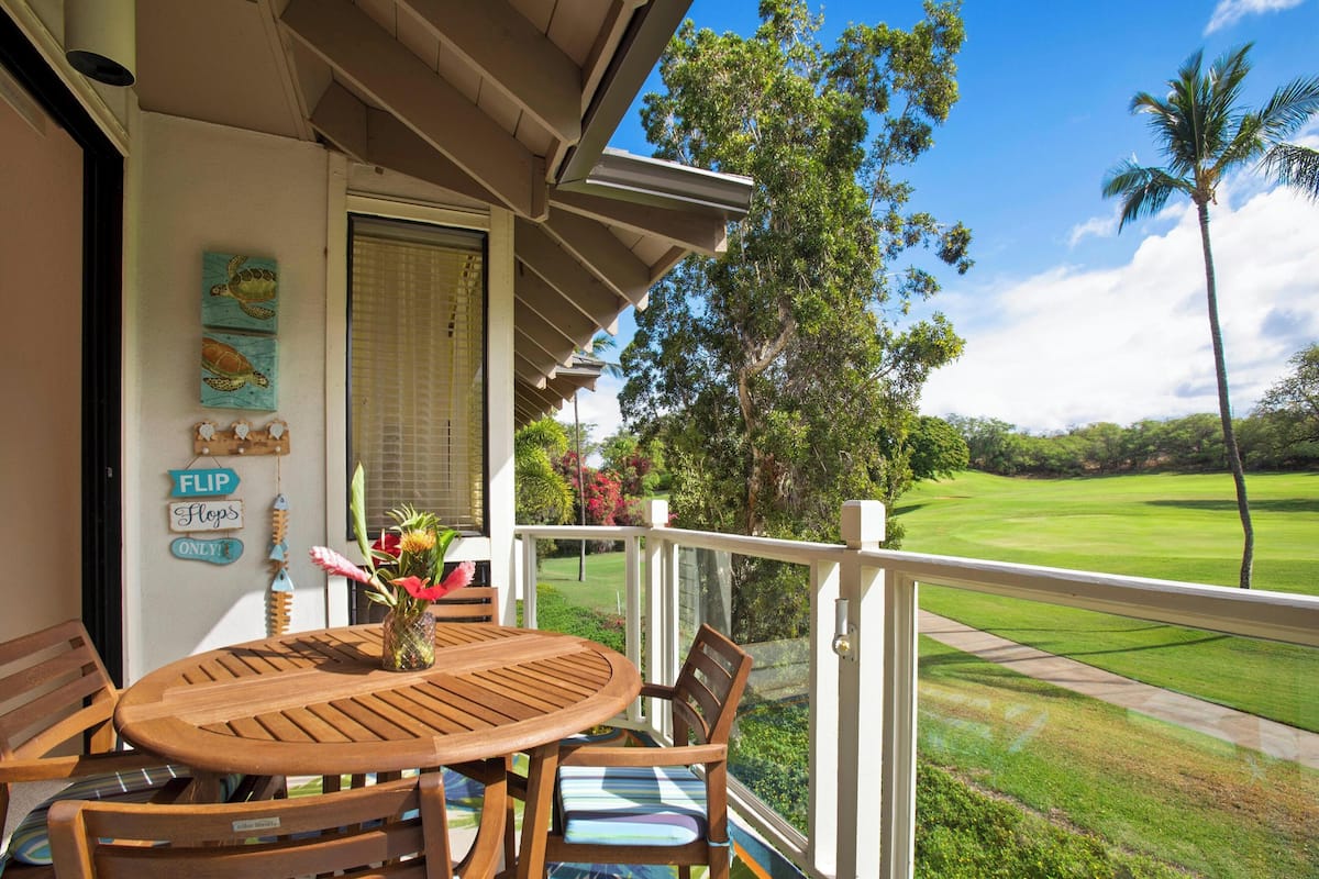 A wooden table and chairs on a balcony with a view of a golf course.