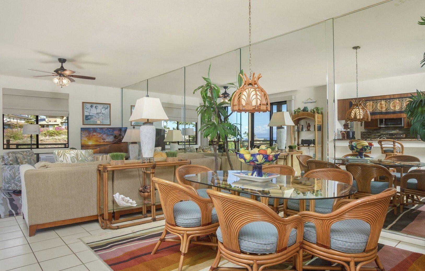 A spacious living room with a glass dining table, wicker chairs, and a ceiling fan.