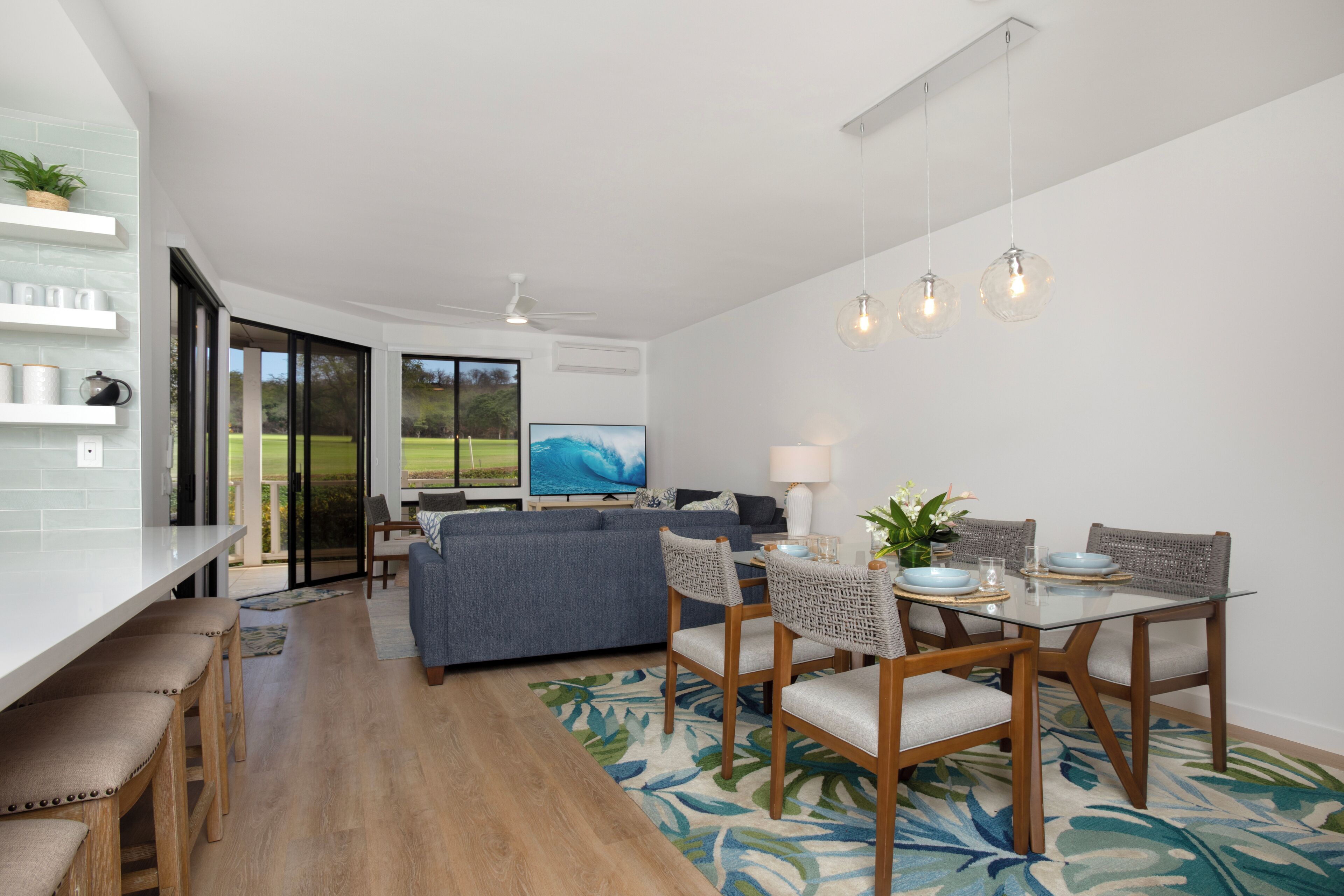 A modern living room with a dining area, a large TV, and a view of the outdoors.