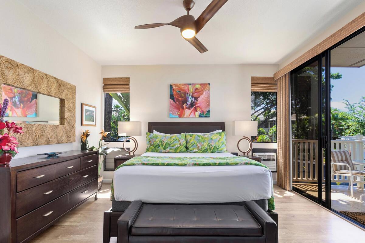 A modern bedroom with a large bed, a ceiling fan, and a view of the outdoors through a sliding glass door.