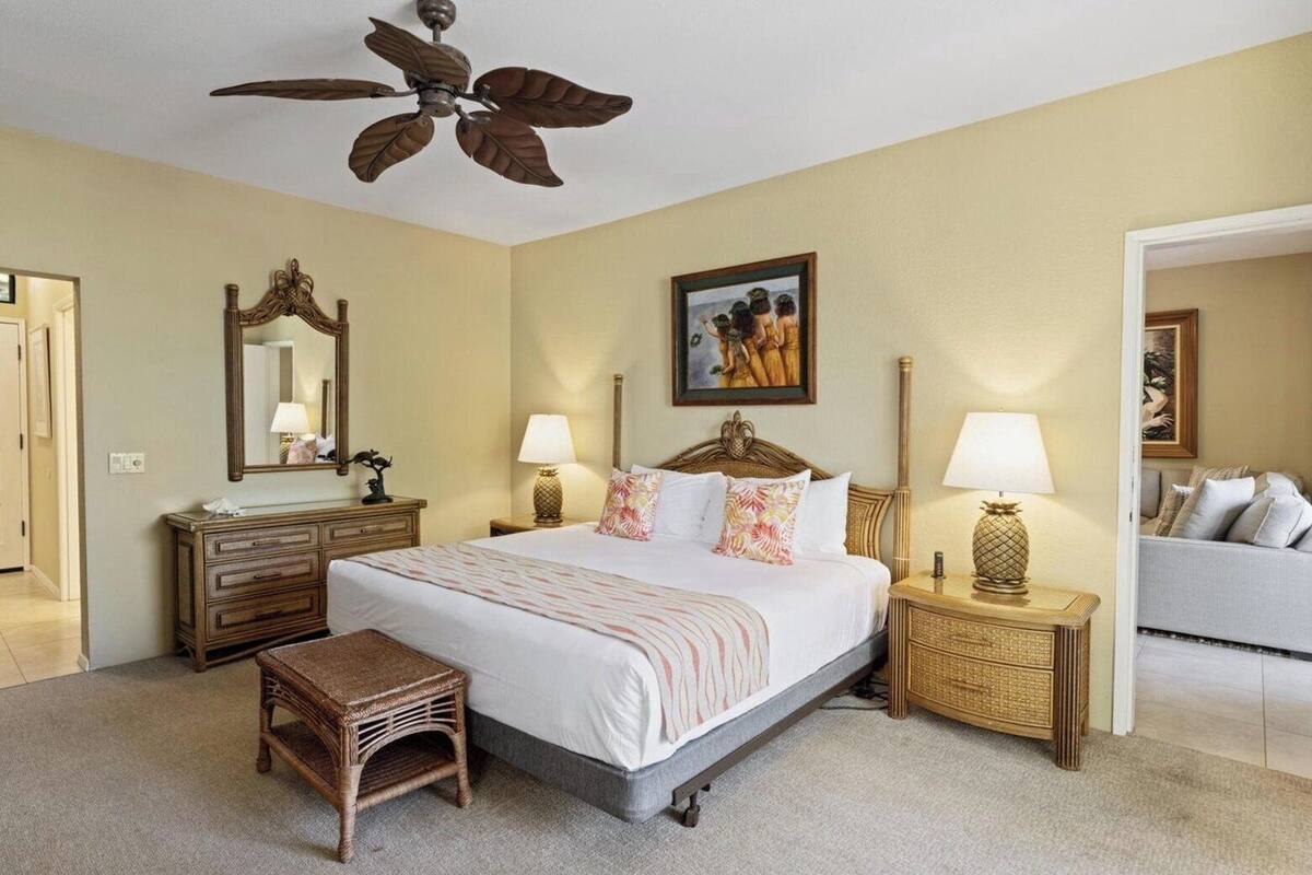 A hotel room with a bed, a nightstand, a lamp, a mirror, a picture on the wall, and a door leading to another room.