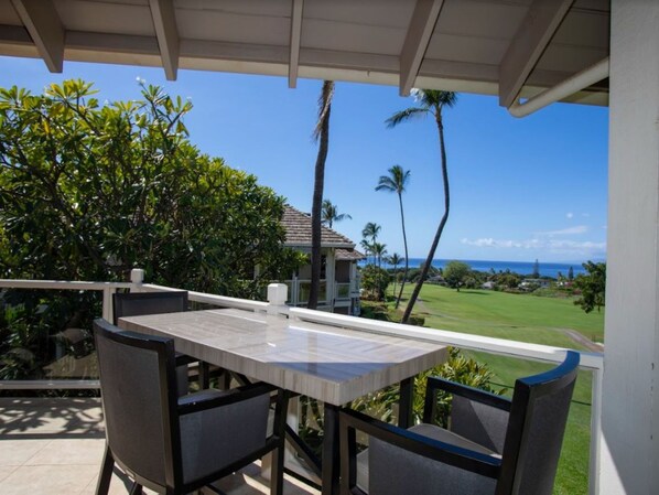 A covered outdoor seating area with a table and chairs, overlooking a golf course and the ocean.