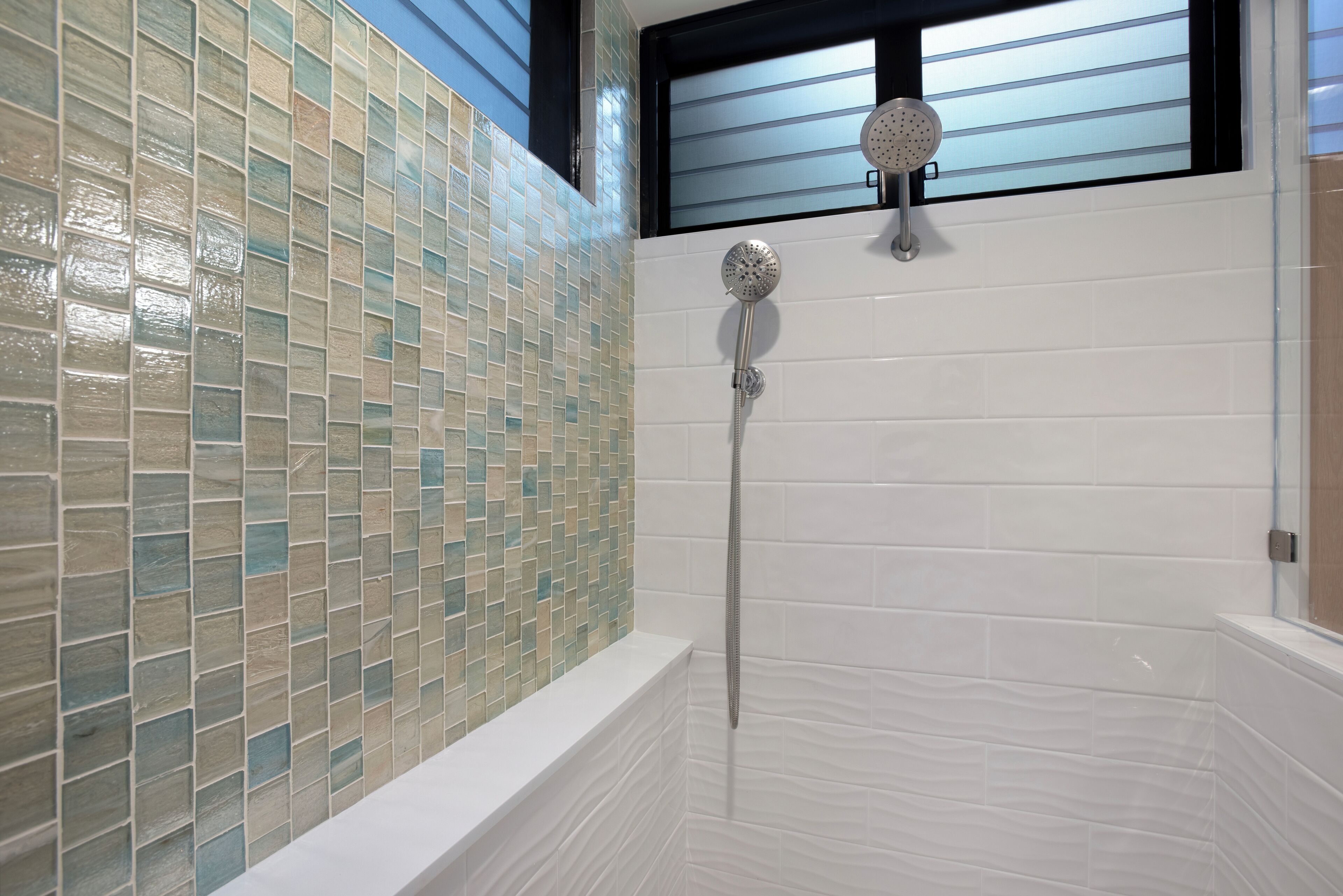 A bathroom with a mosaic tile wall, a showerhead, and a white bathtub.