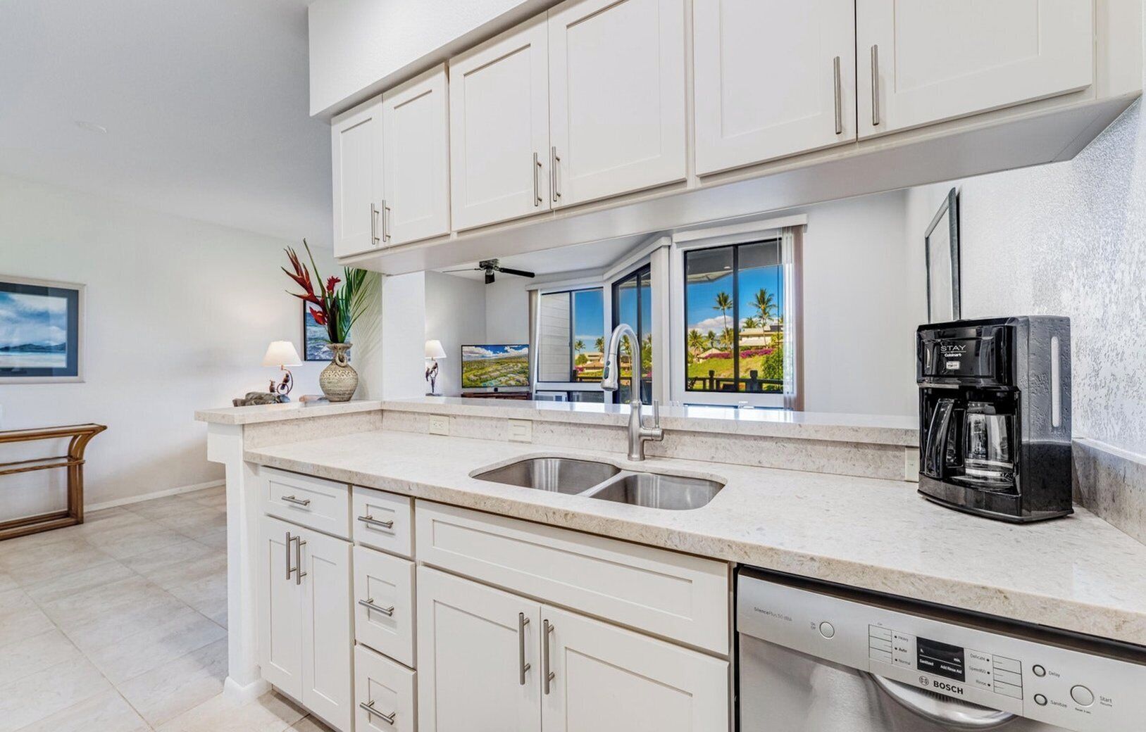 A modern kitchen with white cabinetry, a stainless steel sink, a Bosch dishwasher, and a coffee maker.