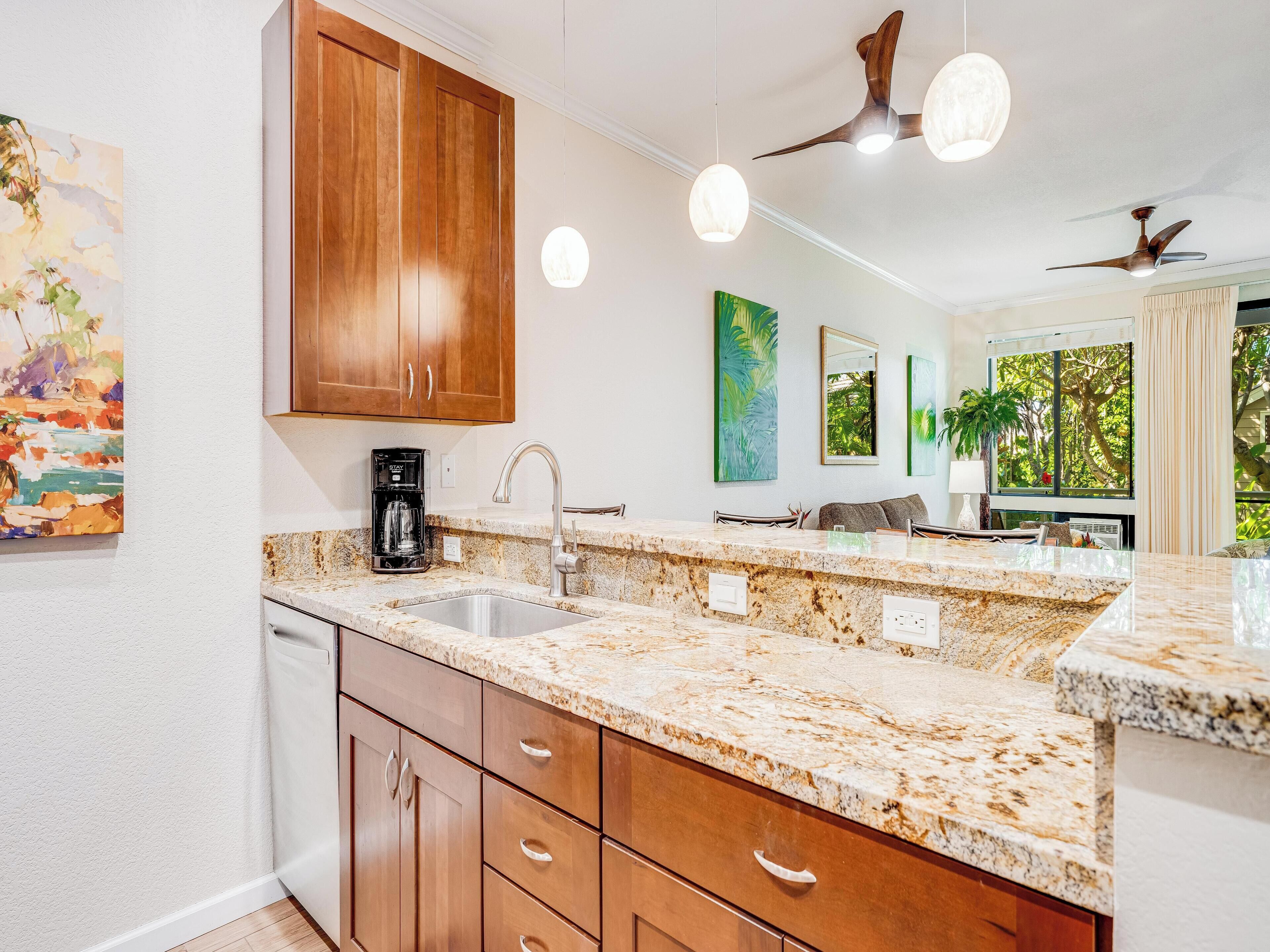 A modern kitchen with granite countertops, wooden cabinets, and a built-in island. There are pendant lights, a ceiling fan, and artwork on the walls.