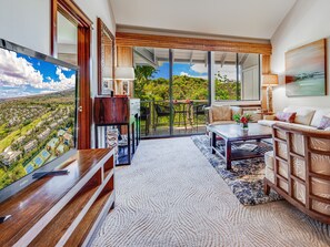 A modern living room with a large TV, comfortable seating, and a view of a residential area.
