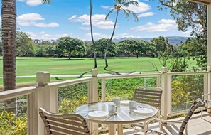Een overdekt terras met een tafel en stoelen, met uitzicht op een golfbaan.