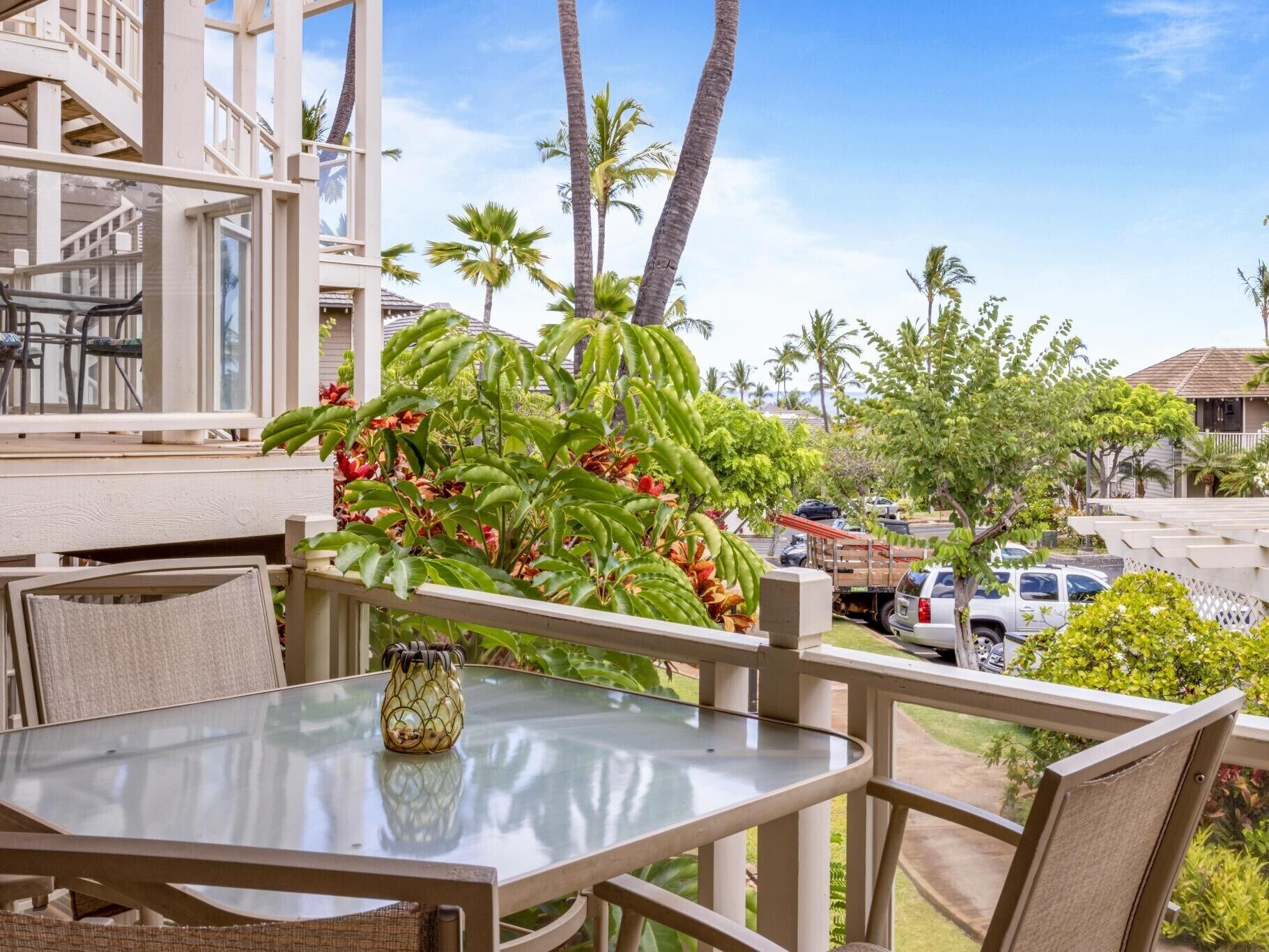 A balcony with a glass table, chairs, and a potted plant.