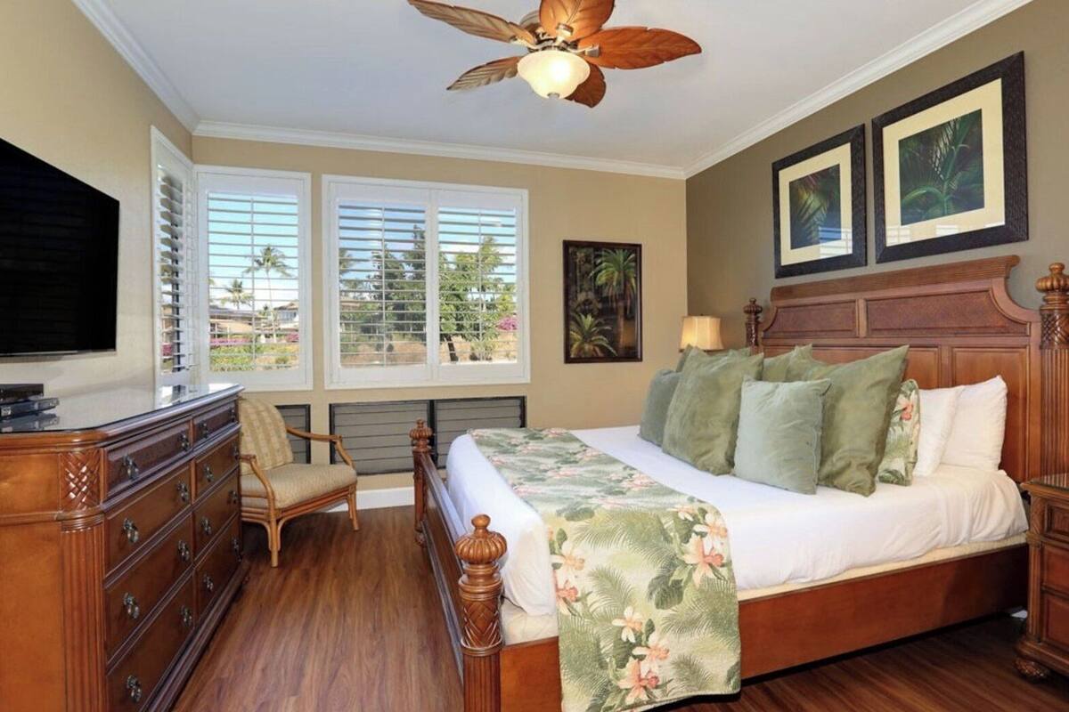 A bedroom with a bed, a dresser, a chair, a ceiling fan, and a TV.