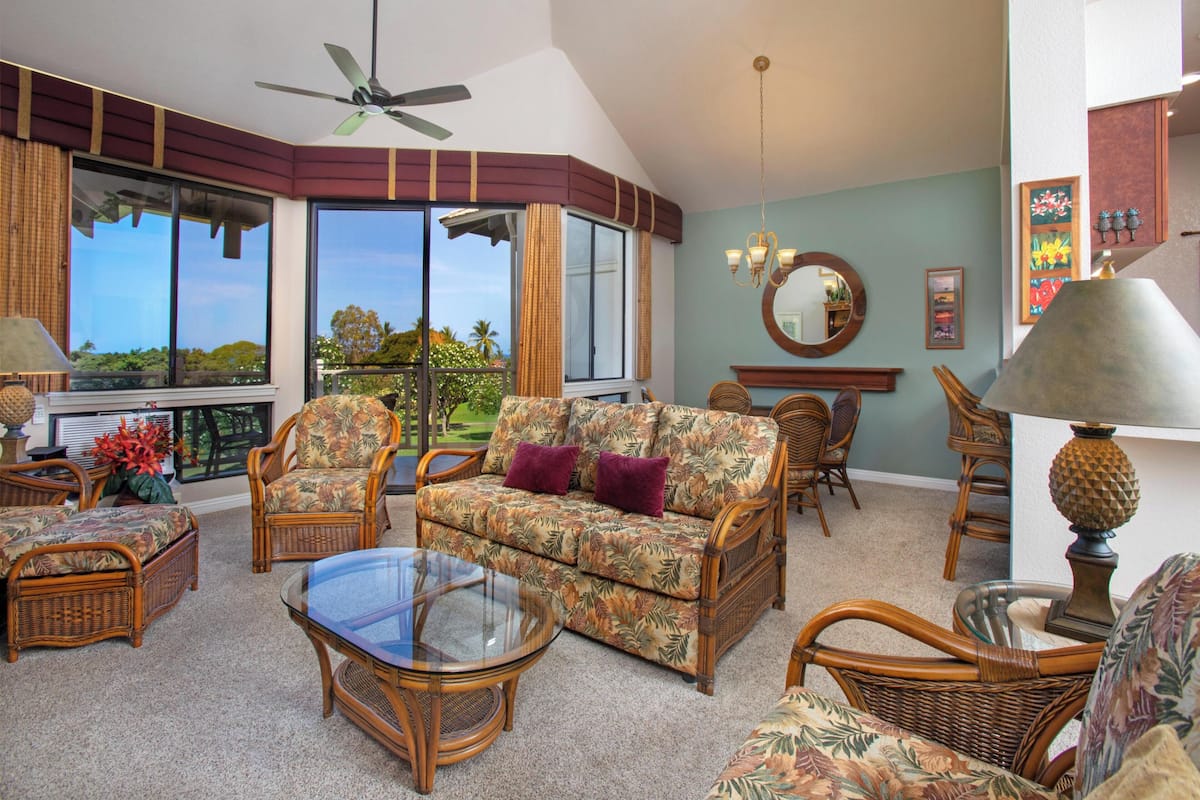 A spacious living area with a large glass table, wicker furniture, and a view of the outdoors.