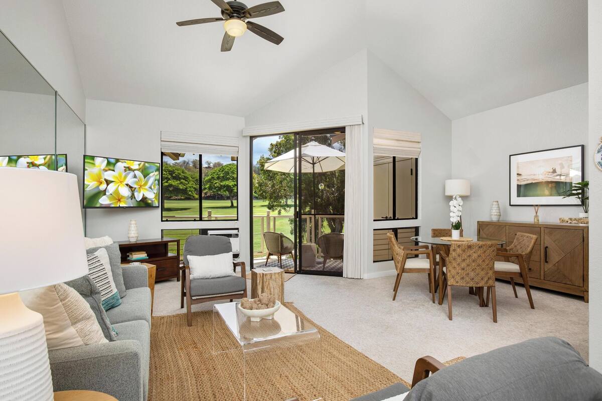 A spacious living area with a large window, a ceiling fan, and a dining table with wicker chairs.