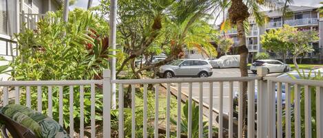 Un balcon donnant sur une rue, entouré de verdure et de palmiers.
