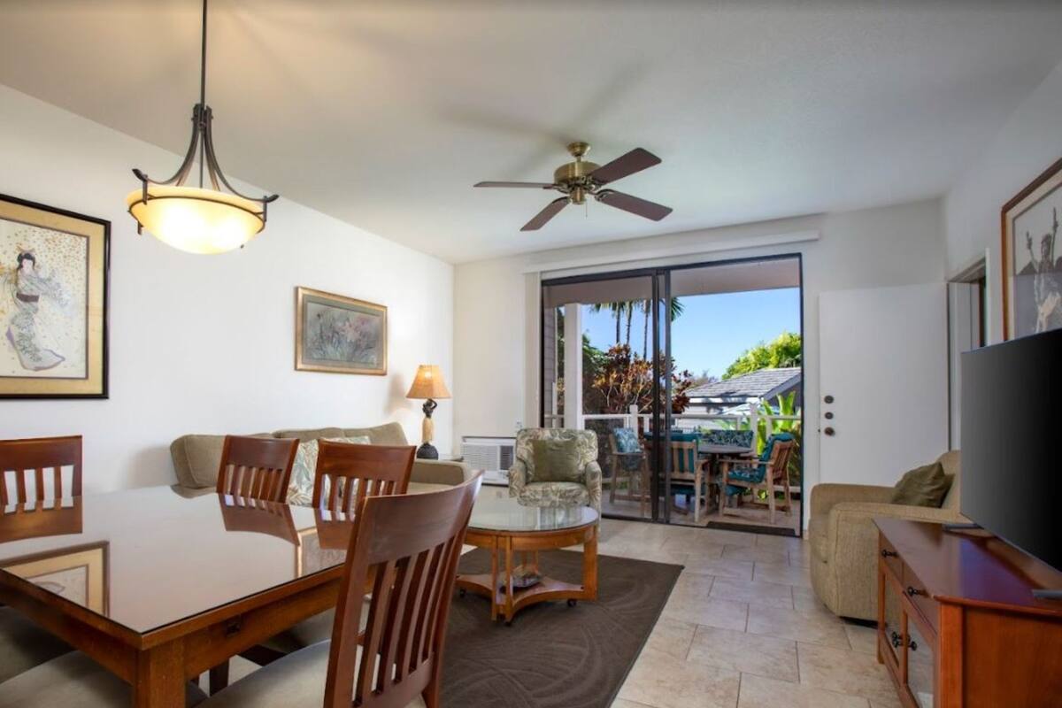 A dining area with a table and chairs, a sofa, a ceiling fan, and a TV.