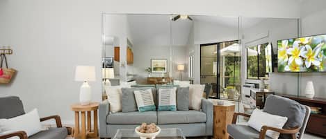 A modern living room with a grey sofa, two armchairs, a coffee table, and a large mirror.