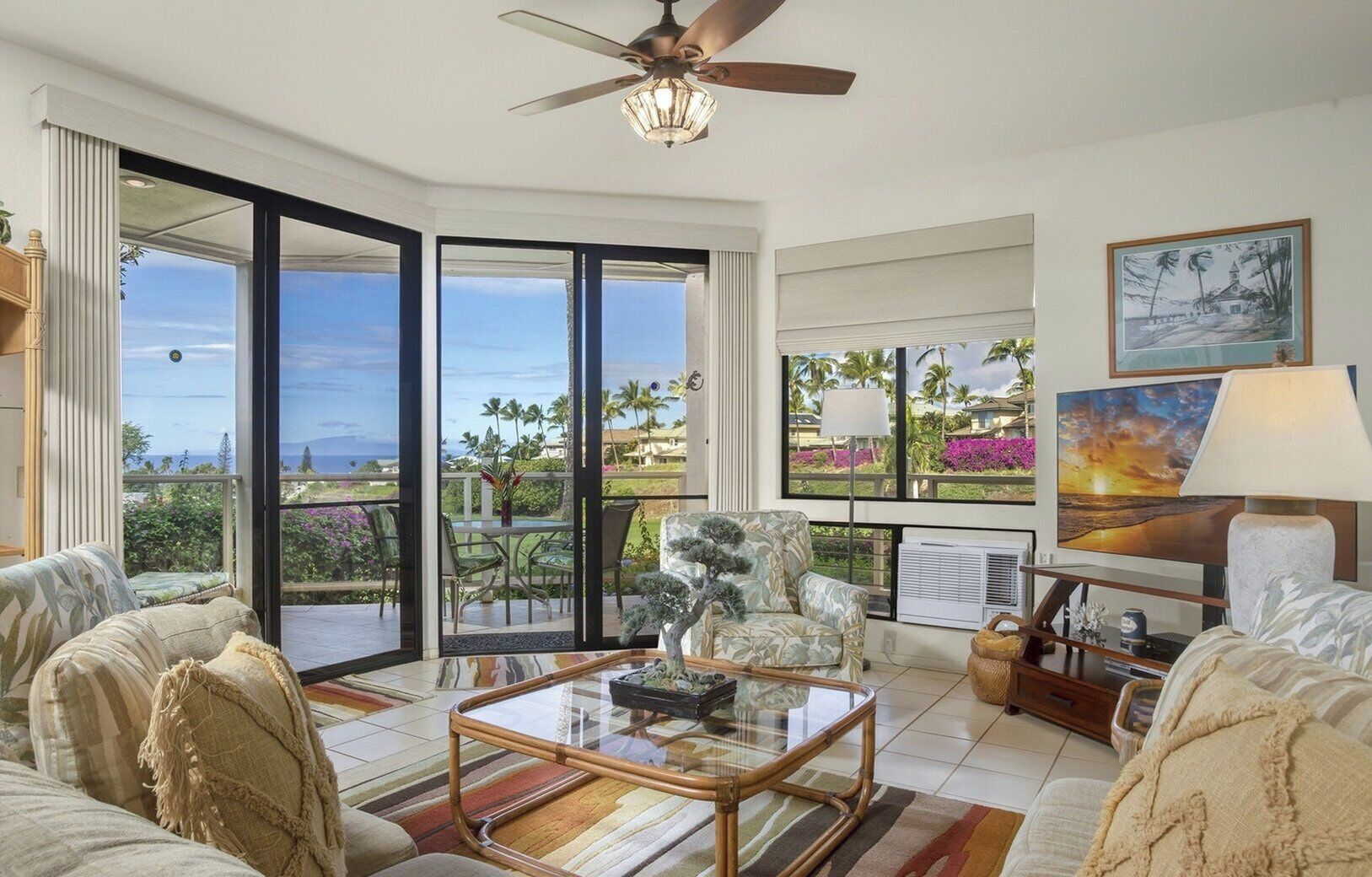 A spacious living room with a large glass door leading to a balcony, a ceiling fan, and a painting on the wall.