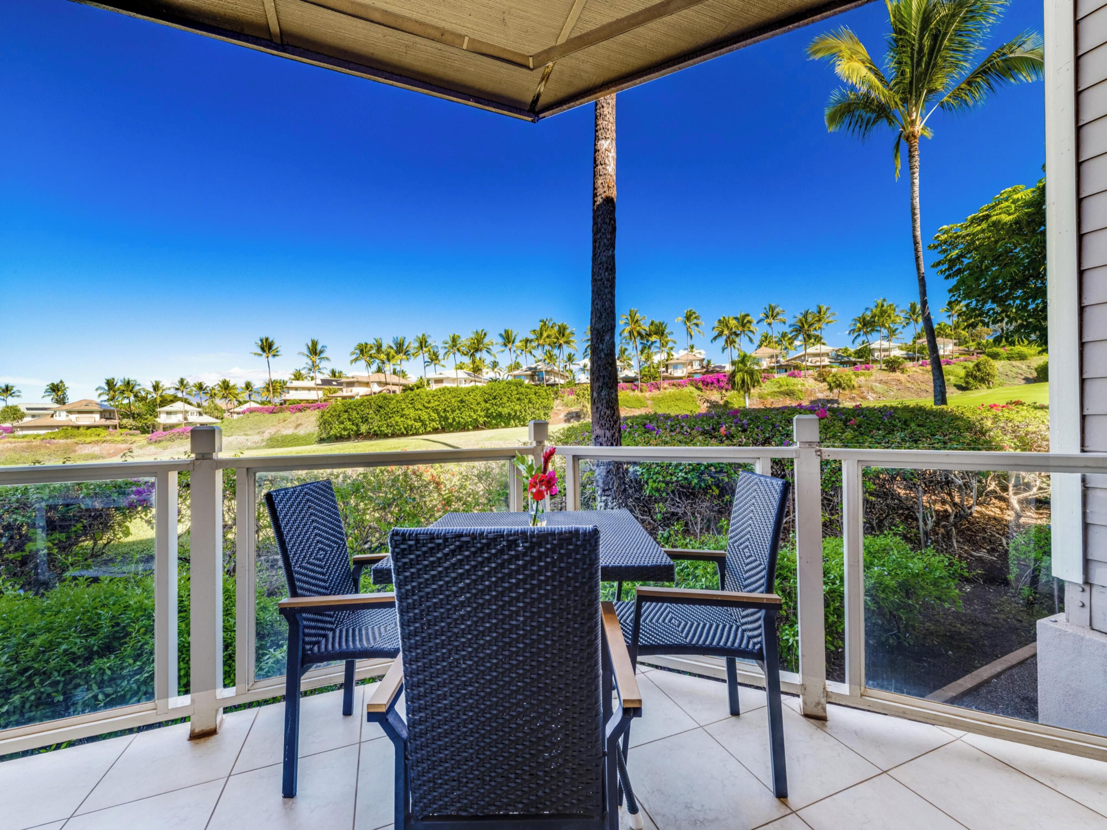 A covered outdoor seating area with a view of a golf course and palm trees.