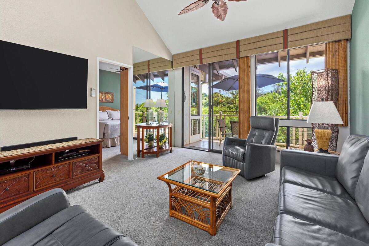 A spacious living room with a flat-screen TV, leather sofa, and a glass coffee table.