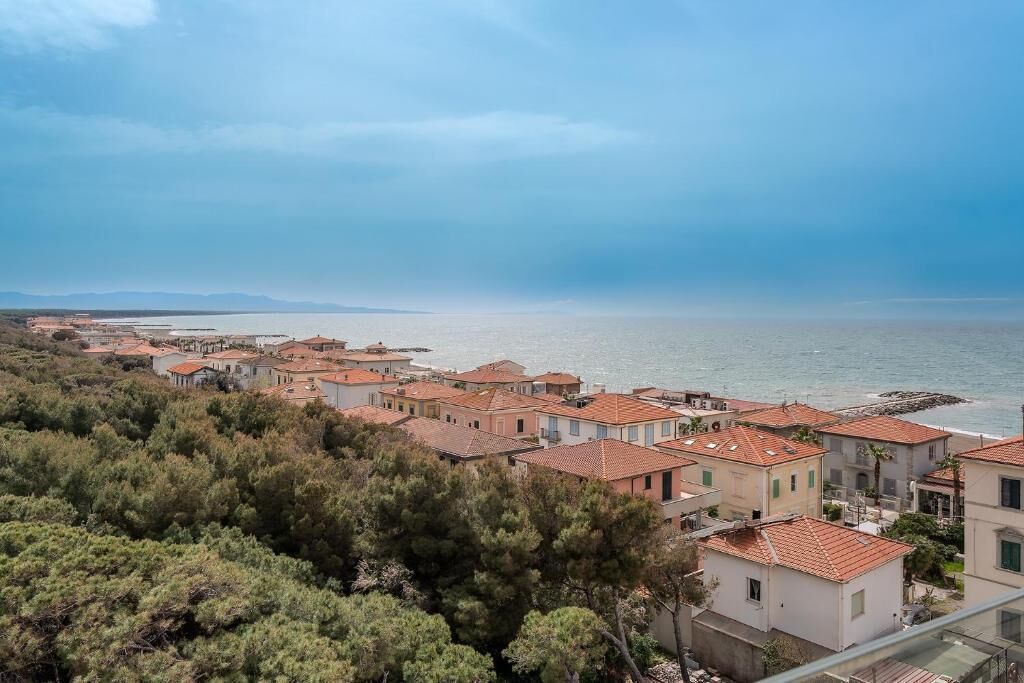 Zona residencial costera con casas de tejados de teja, vista al mar y una cadena montañosa distante.