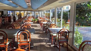 Ein geräumiges Restaurant mit hohen Decken, blauen und weißen Streifenpaneelen an der Decke und großen Fenstern mit Blick auf einen Garten.