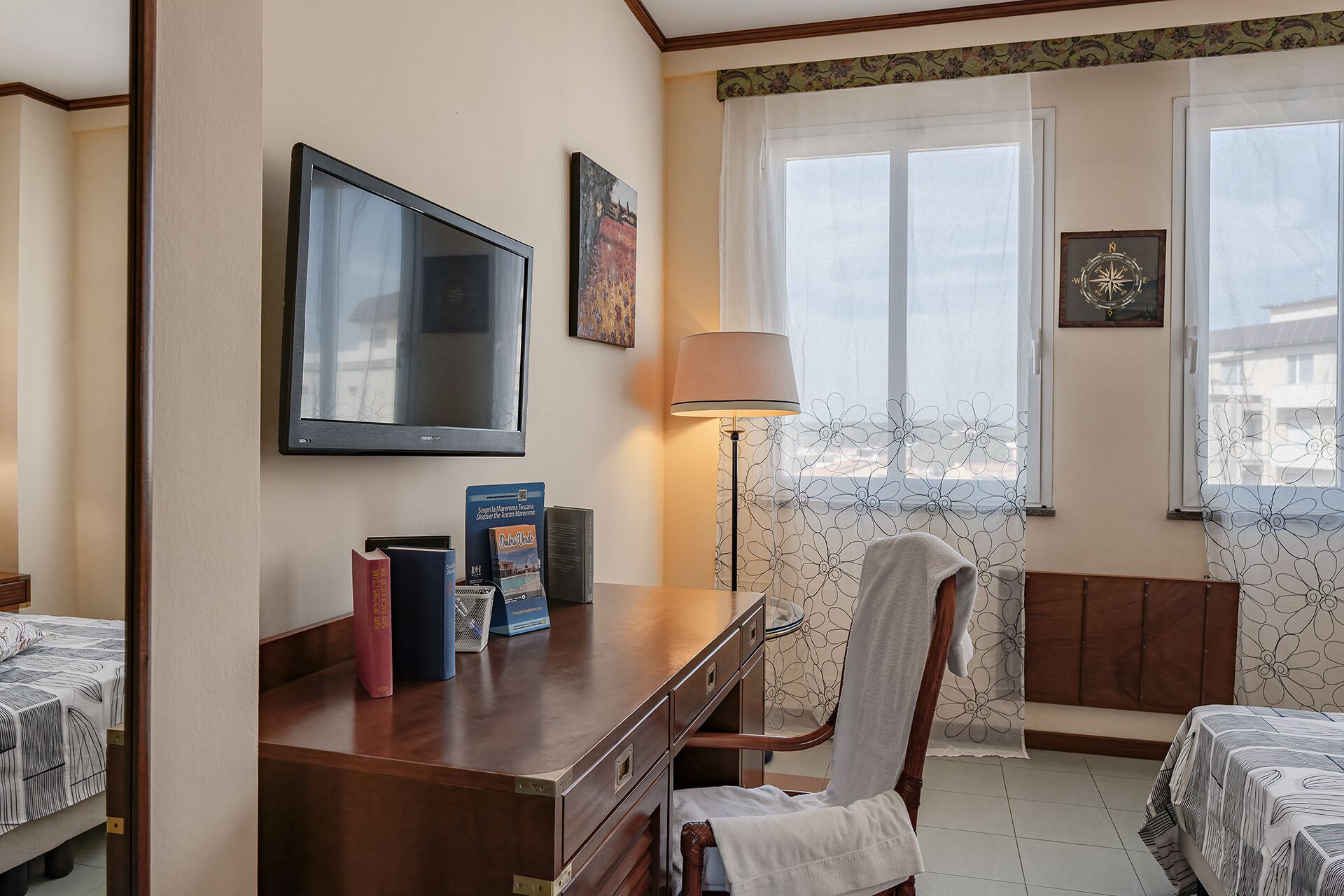 Ein Hotelzimmer mit einem Bett, einem Schreibtisch mit Büchern, einer Lampe und einem Fernseher.