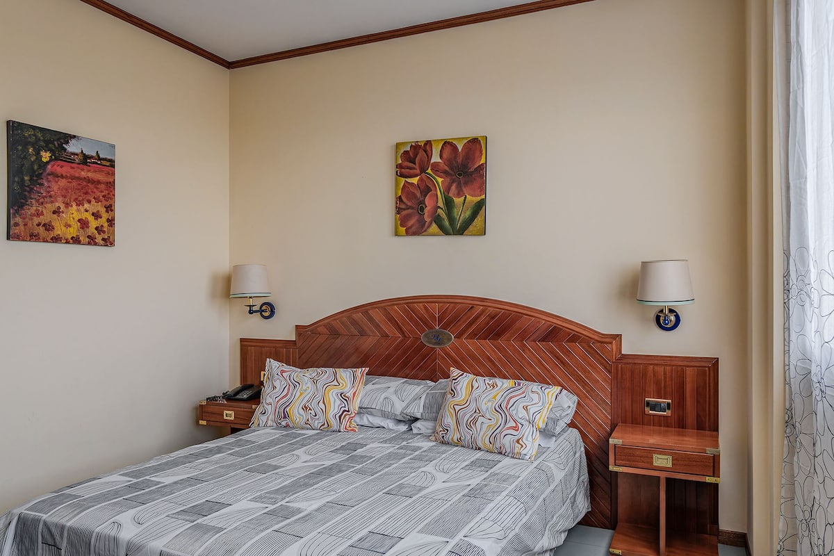 Una habitación de hotel con una cama, dos mesitas de noche, una lámpara y dos lámparas de pared.