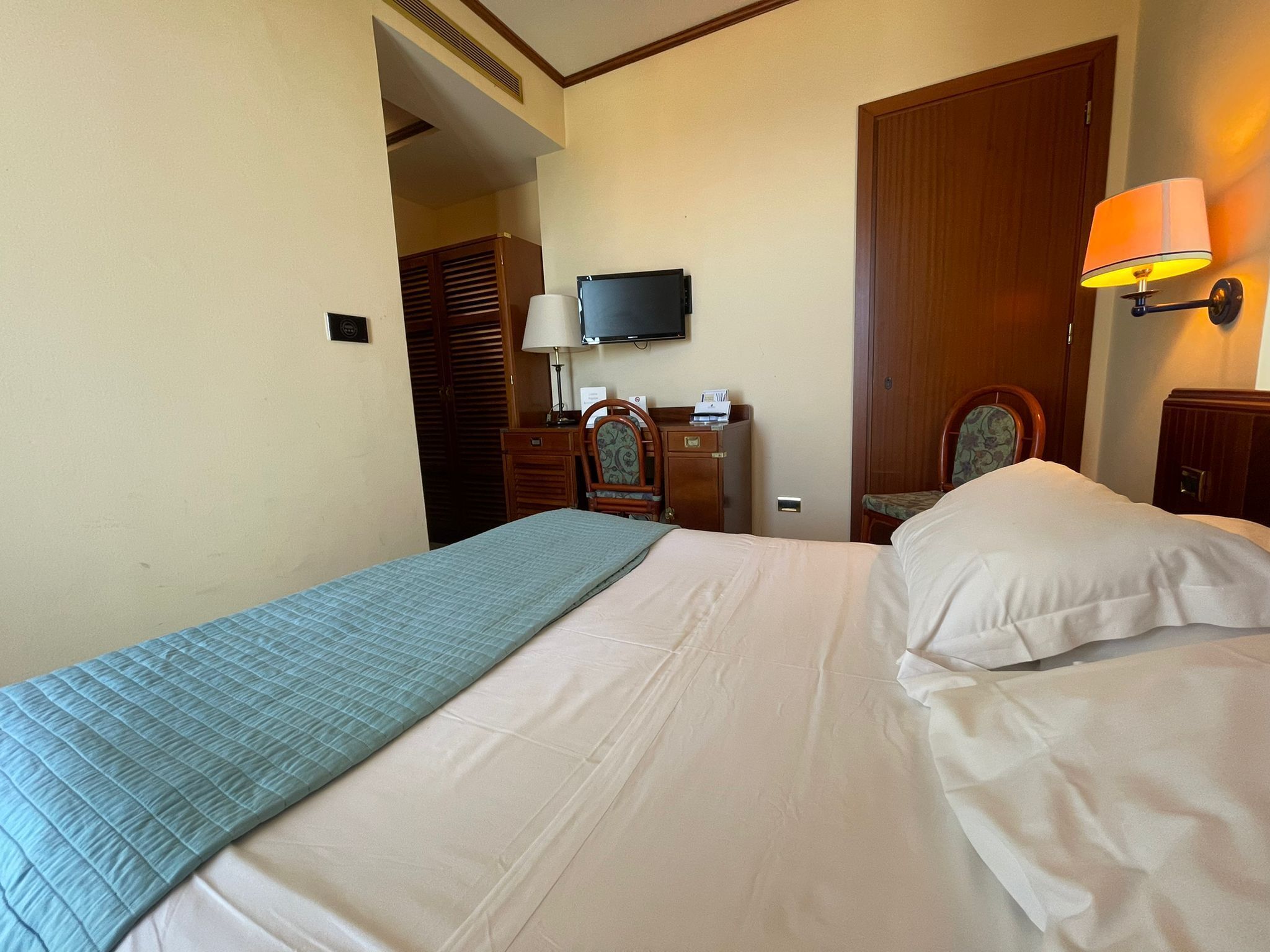 A hotel room with a bed, a television, a desk with a chair, and a lamp.