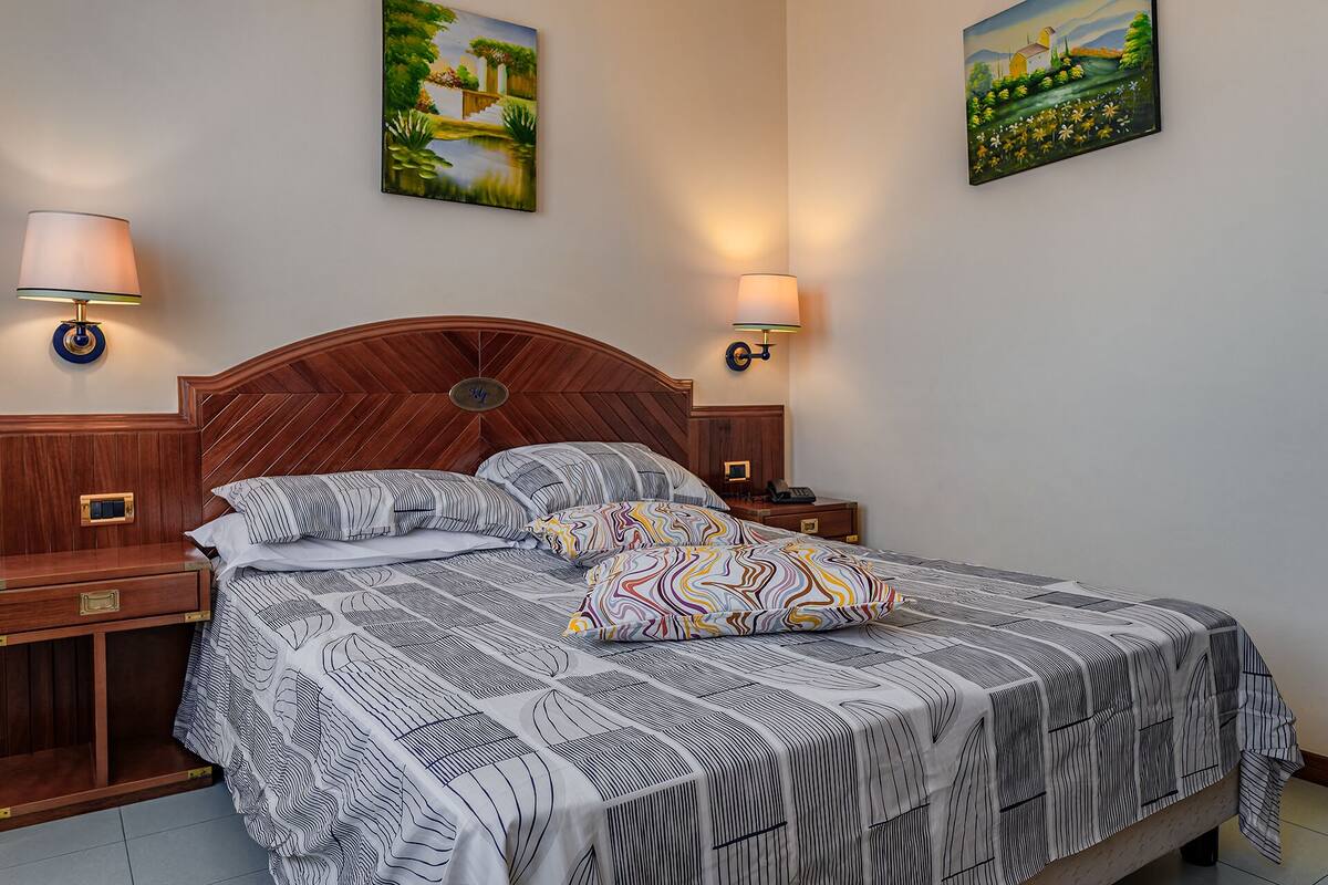 Una cama bien hecha con ropa de cama a rayas, dos mesitas de noche con lámparas y dos cuadros en las paredes.